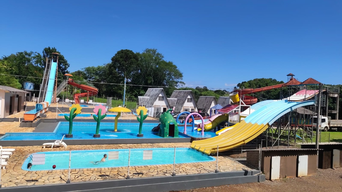 Vista ampla do parque aquático com piscinas, brinquedos e chalés ao fundo